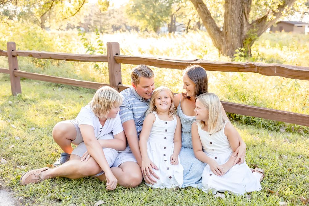 Family members relaxing on grass next to wooden fence during golden hour photography session.