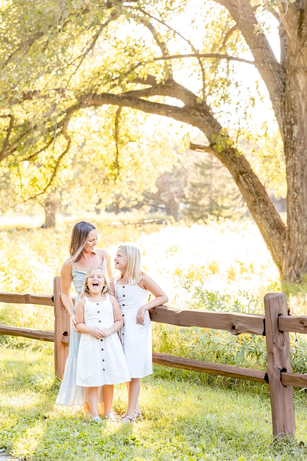Golden hour family photos taken along rustic wooden fence in natural outdoor setting.