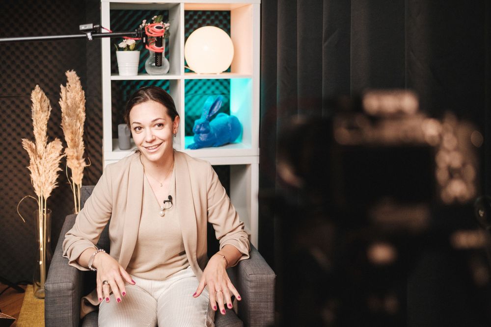 A professional speaker gestures while seated in a modern studio environment.