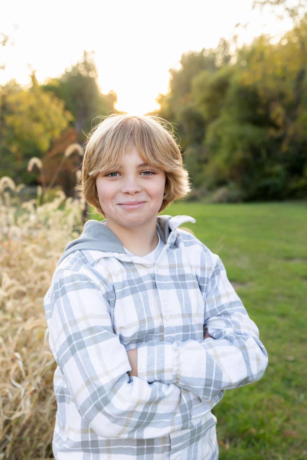 Youth wearing gray plaid hoodie poses confidently in outdoor setting with tall grass.