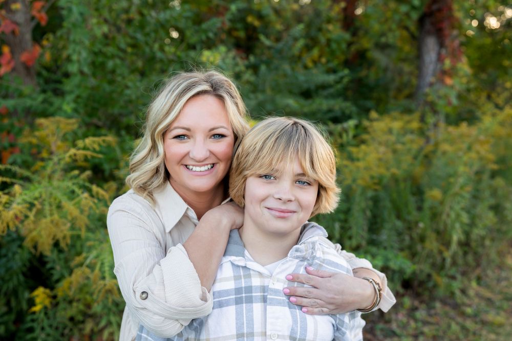 Portrait of two people embracing outdoors with autumn foliage in the background.