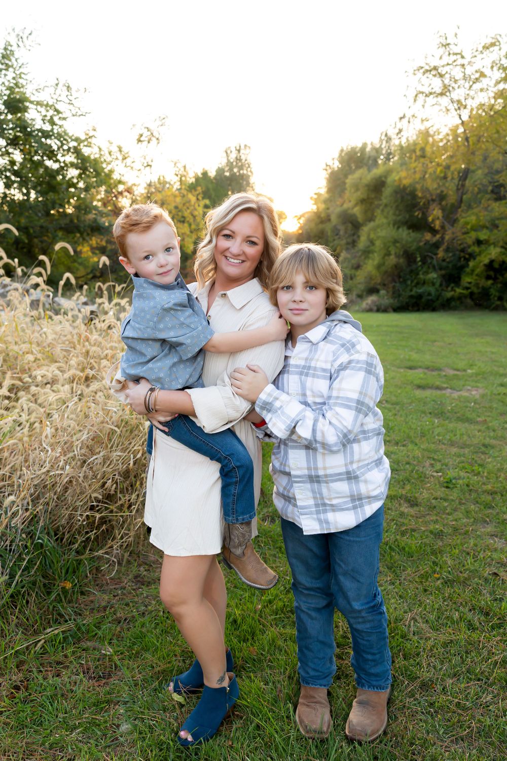 Family portrait outdoors with tall grass and trees in golden evening light.