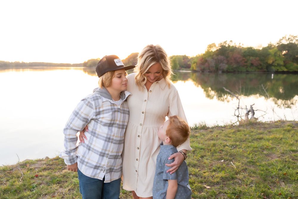 Three people share a moment by a reflective lake at sunset.