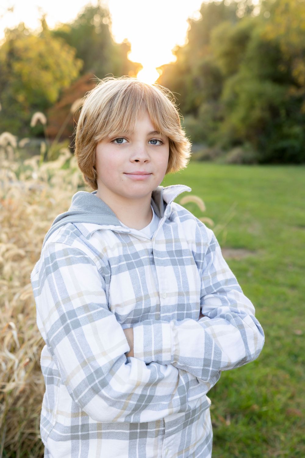 Young person in plaid hoodie standing in golden outdoor setting at sunset.
