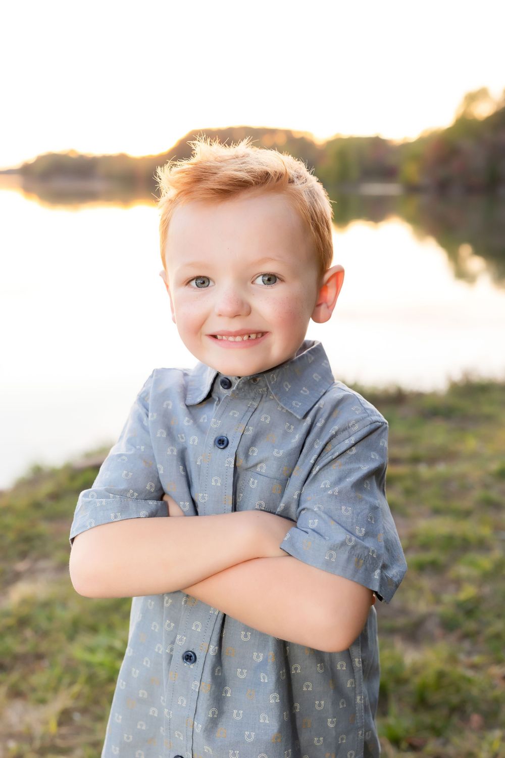 Portrait of child in blue shirt smiling by lake at sunset.