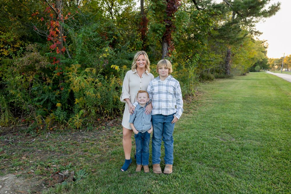 Three people pose together for a family portrait on grass with autumn trees in background.