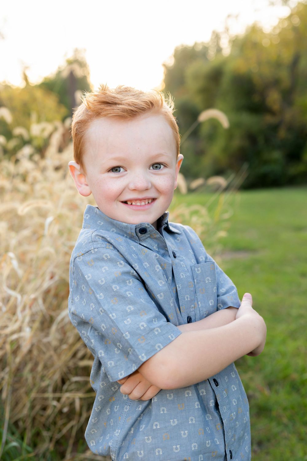 Joyful portrait of child wearing blue patterned shirt against natural backdrop.