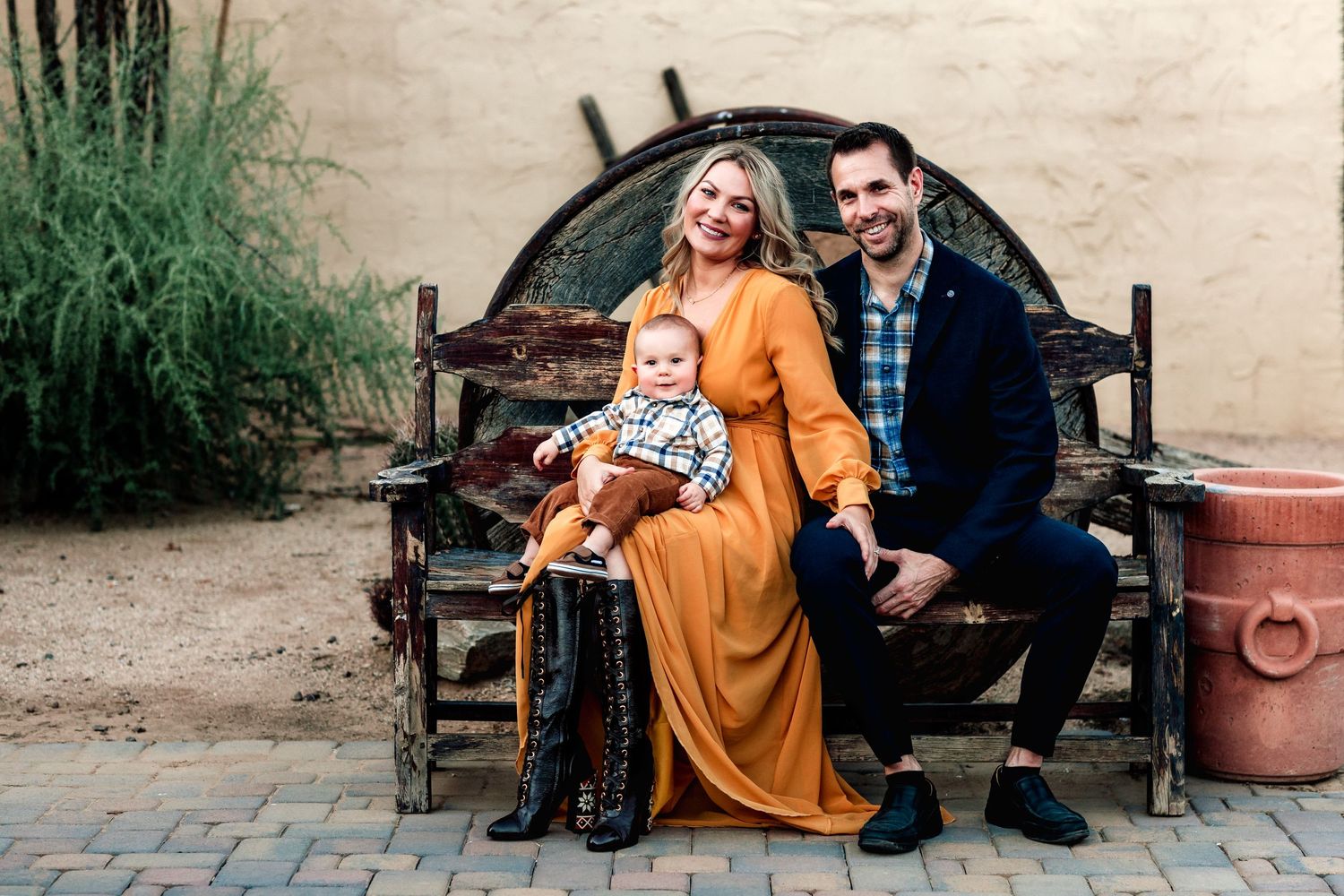 Family sitting together on rustic wooden bench against beige wall with plants.