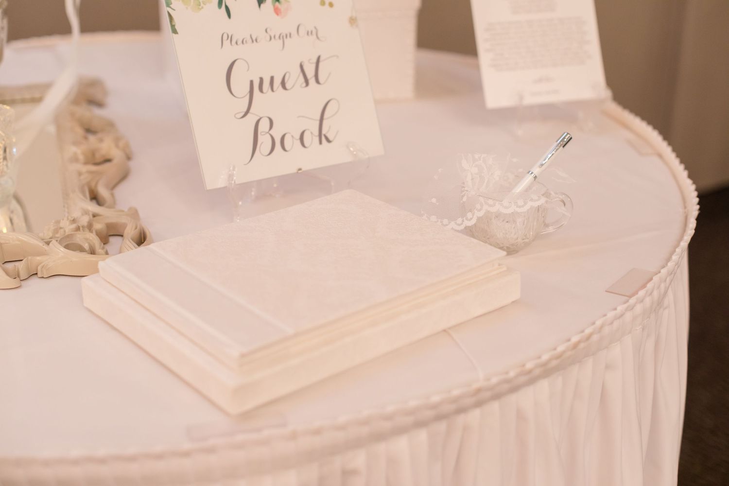 White tablecloth-covered guest book station with decorative signage and writing materials.