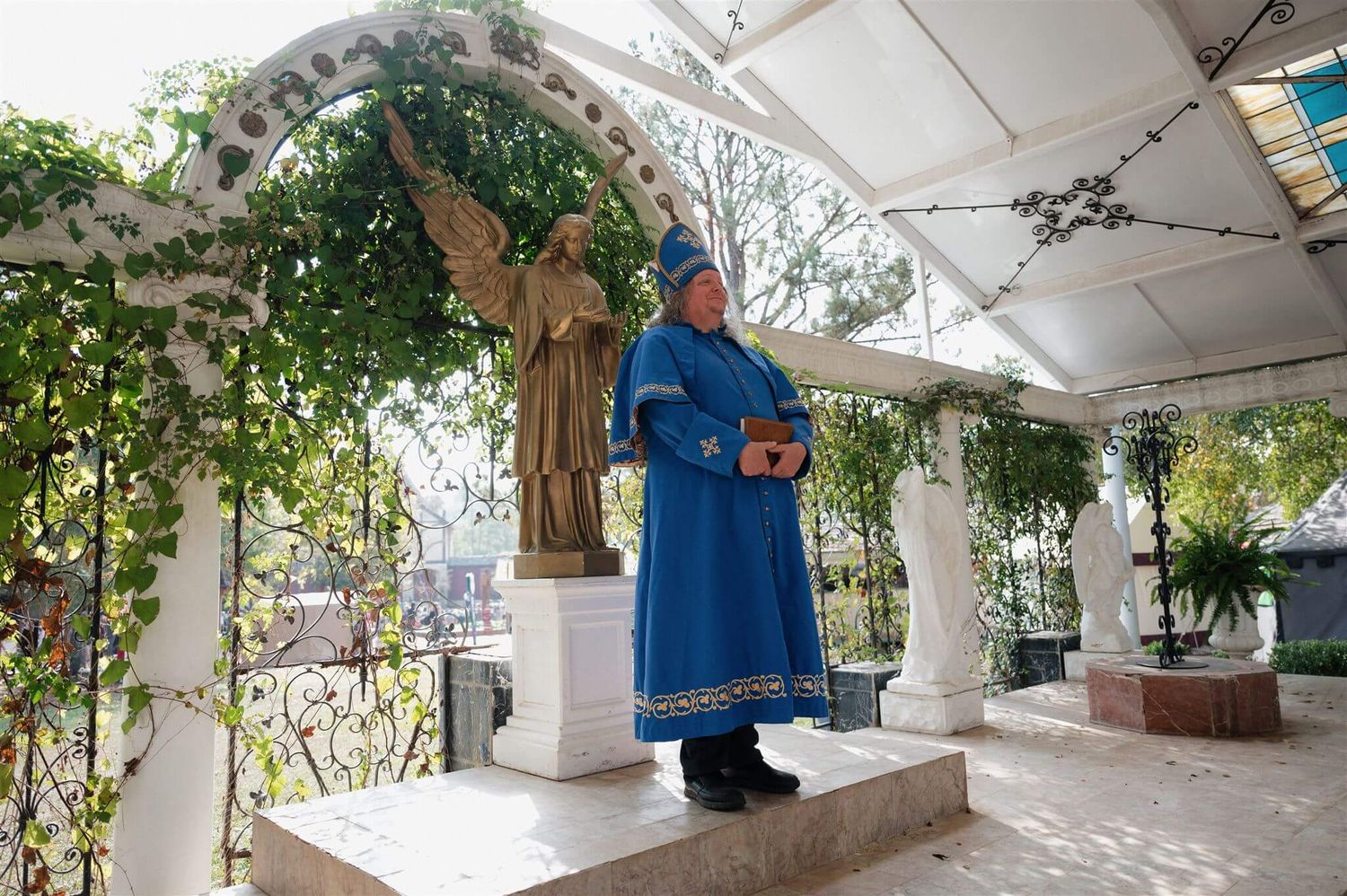 Person in bright blue medieval robes stands on a platform under an ornate white pavilion.