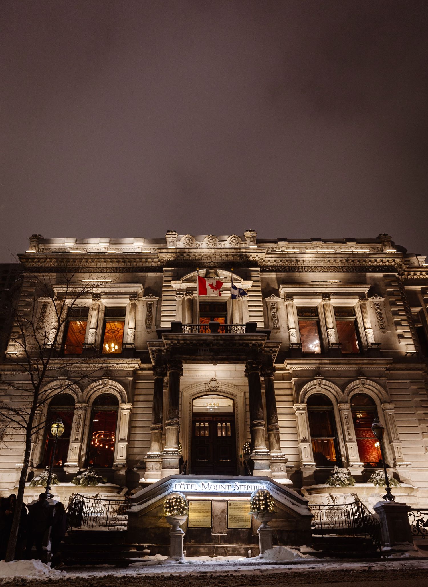 Historic stone building illuminated at night with snow and holiday decorations.