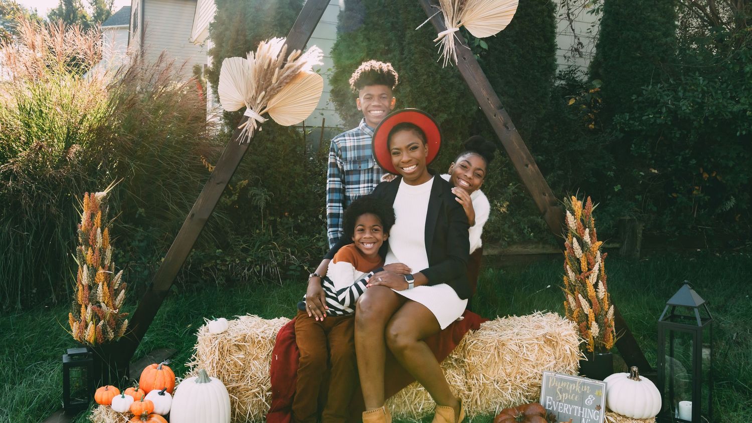 Family posing on hay bales with fall pumpkin decorations outdoors.