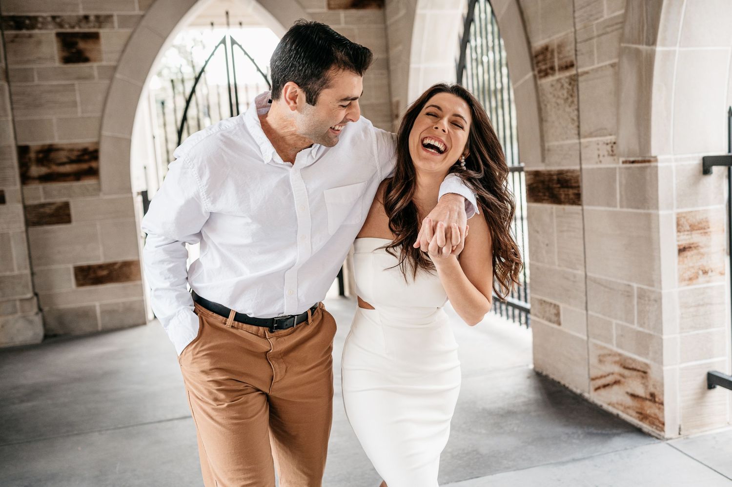 A joyful couple laughing together under stone archways.