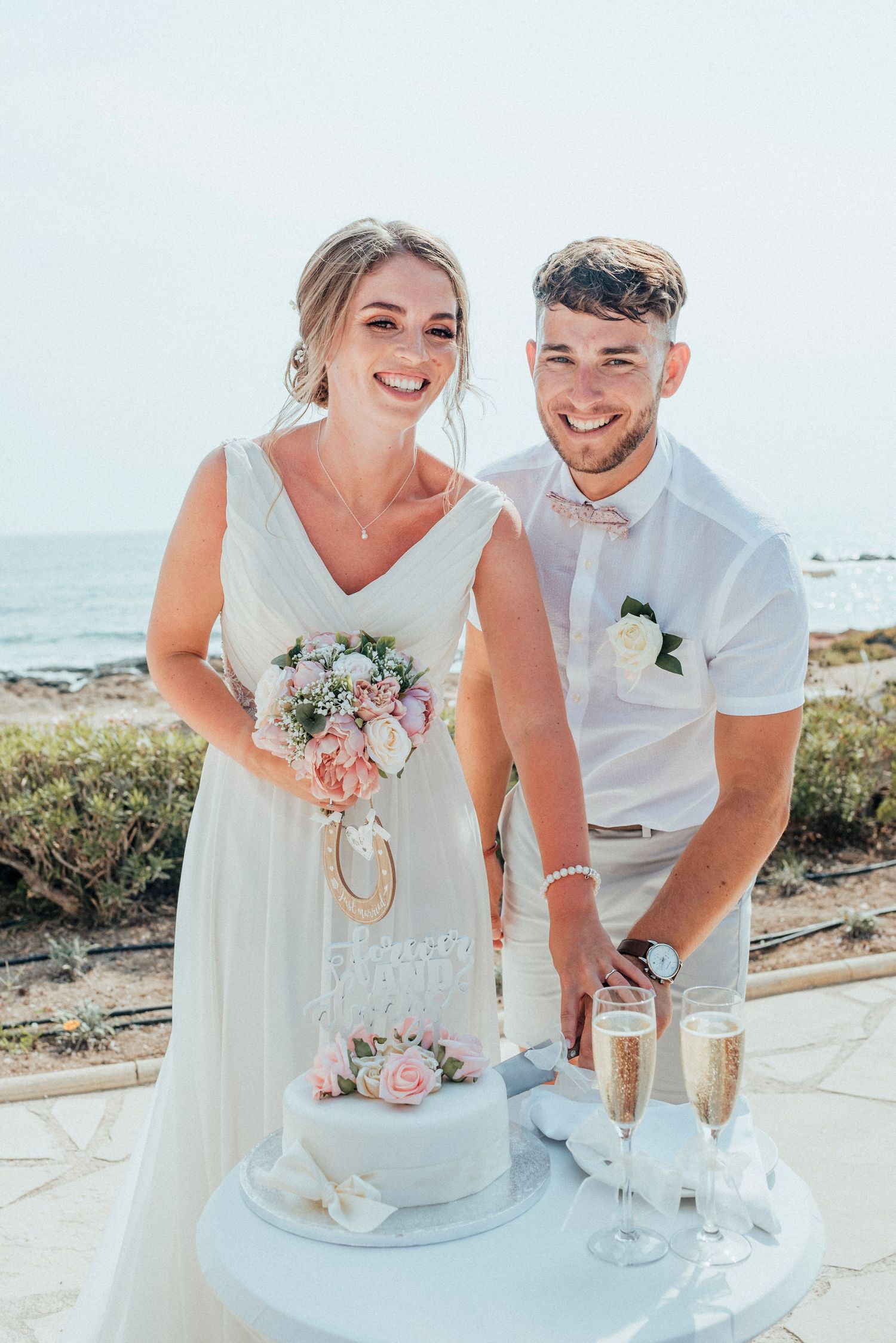 Elegant beachside wedding celebration with cake and champagne set against bright coastal backdrop.