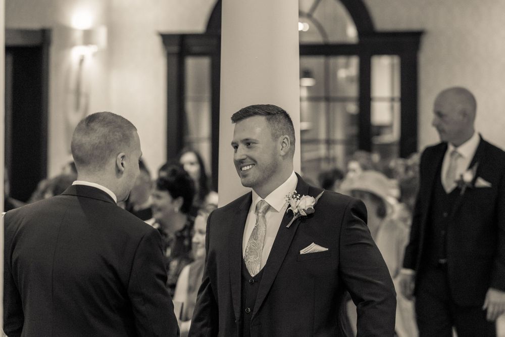 groom smiles chatting to the best man in the ceremony room at the mercure hotel haydock