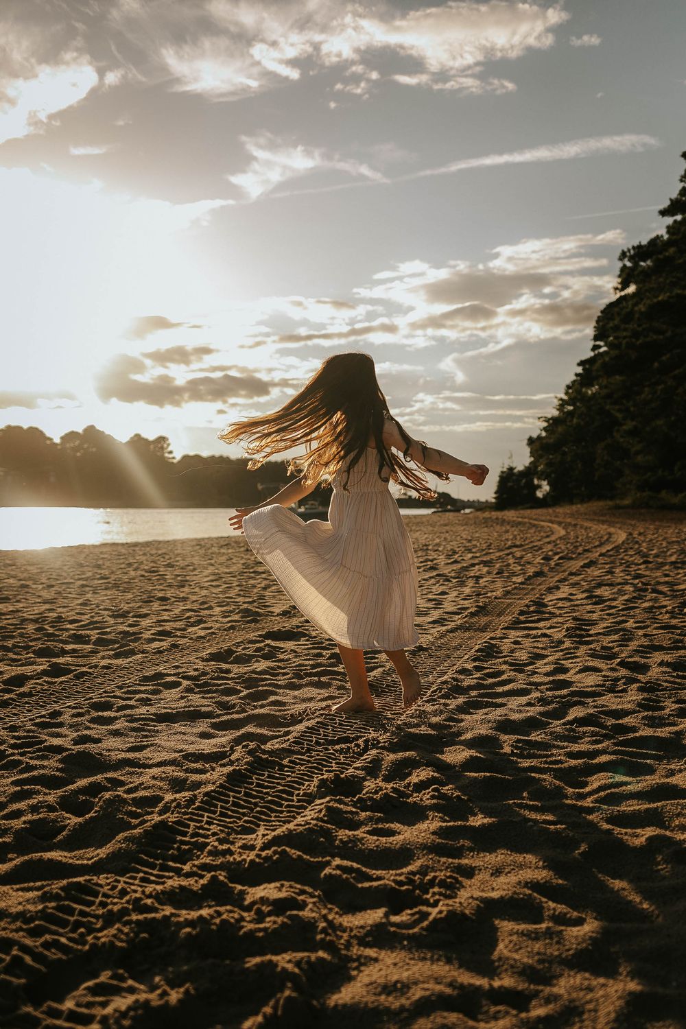 A person in a white dress twirls on a sandy beach during golden hour.