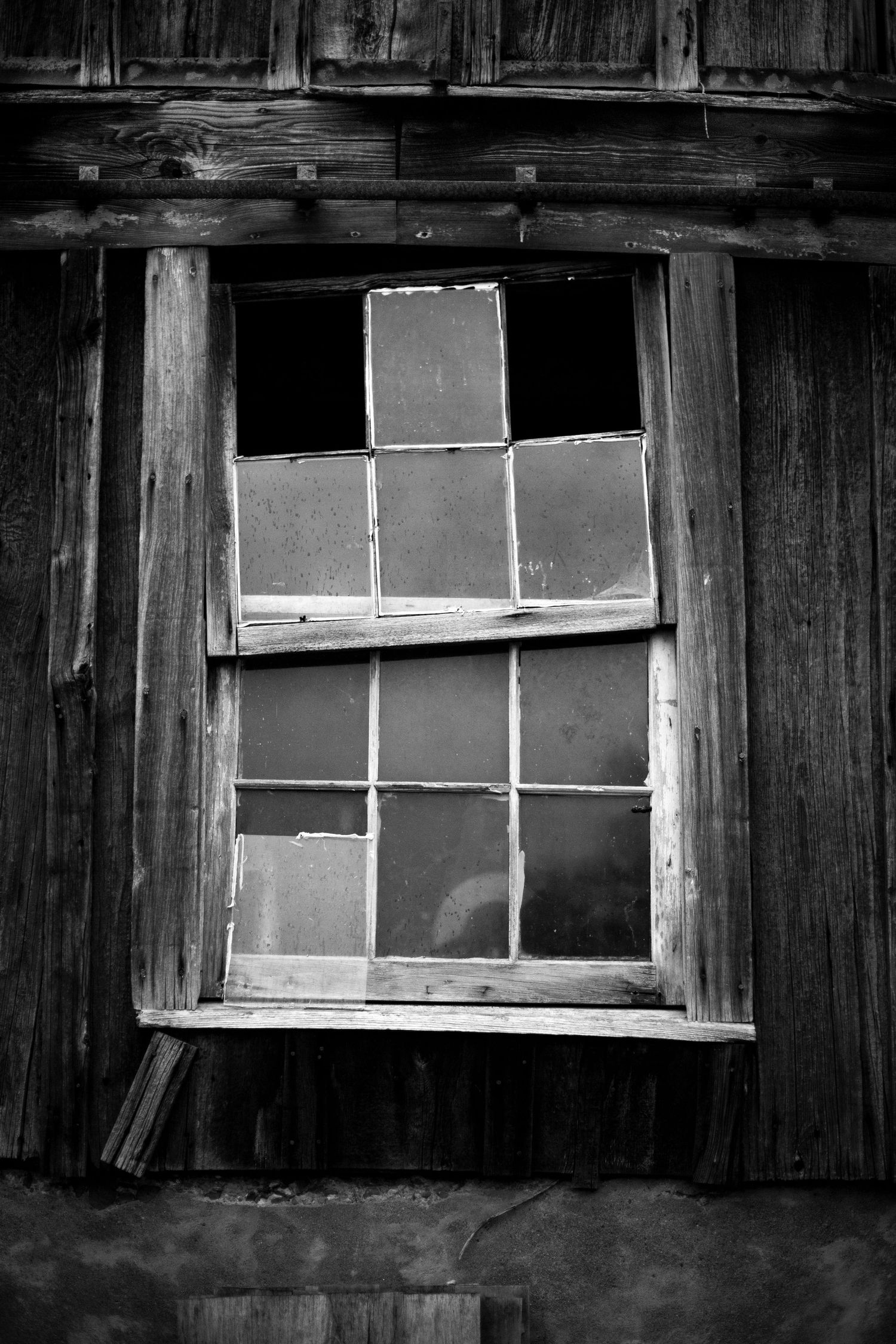 A black and white image of an old crooked window with raindrops on the glass.