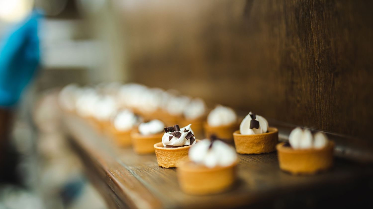 Row of mini tarts topped with whipped cream on a wooden surface.