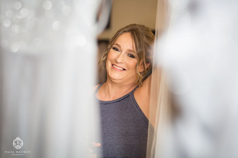Wedding party member smiles joyfully while getting ready in a sunlit room.