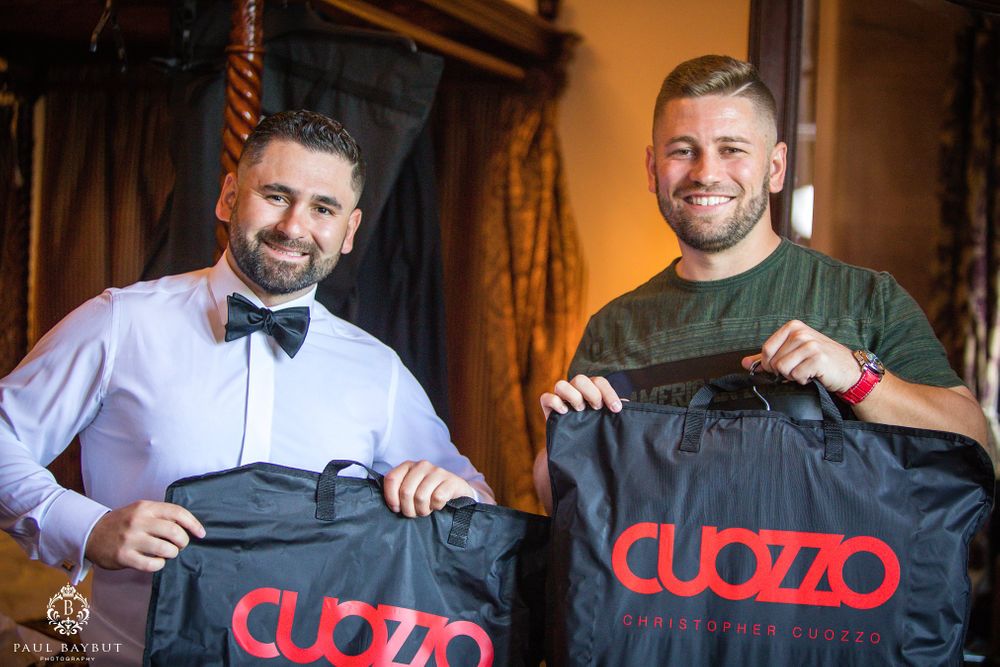 Two men display black t-shirts with Cuozzo branding in formal attire.