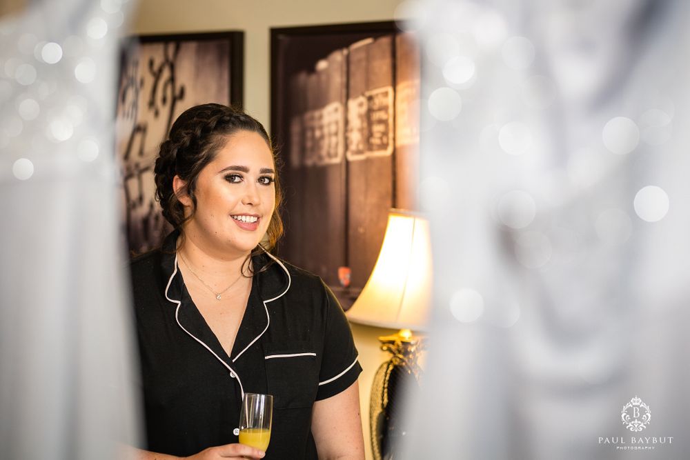Person in black piped pajamas holds champagne glass during pre-event preparations.