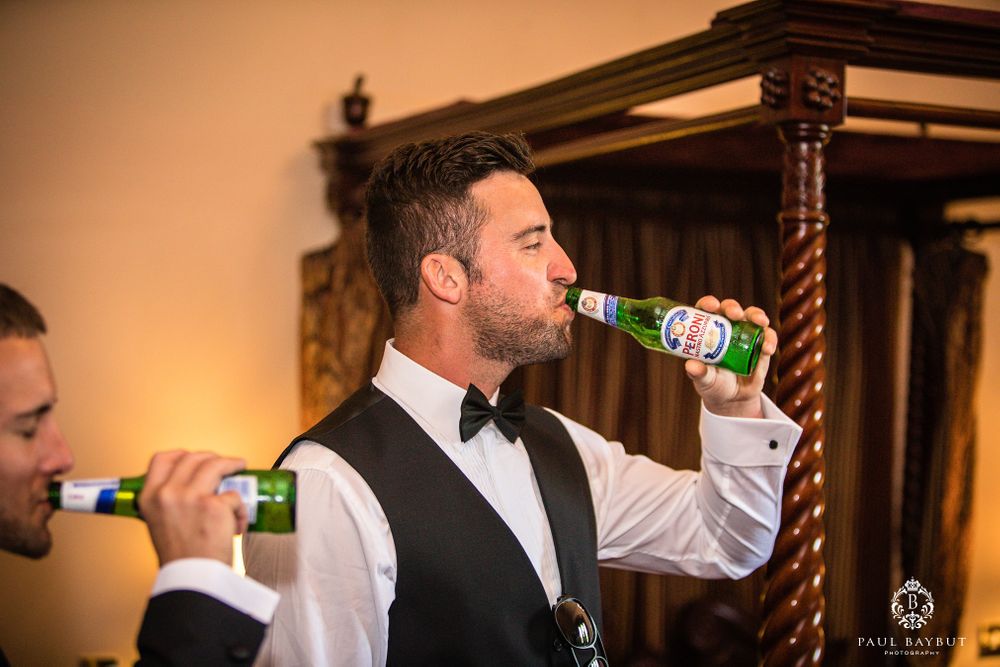 Men in formal attire drinking beer bottles during celebration.