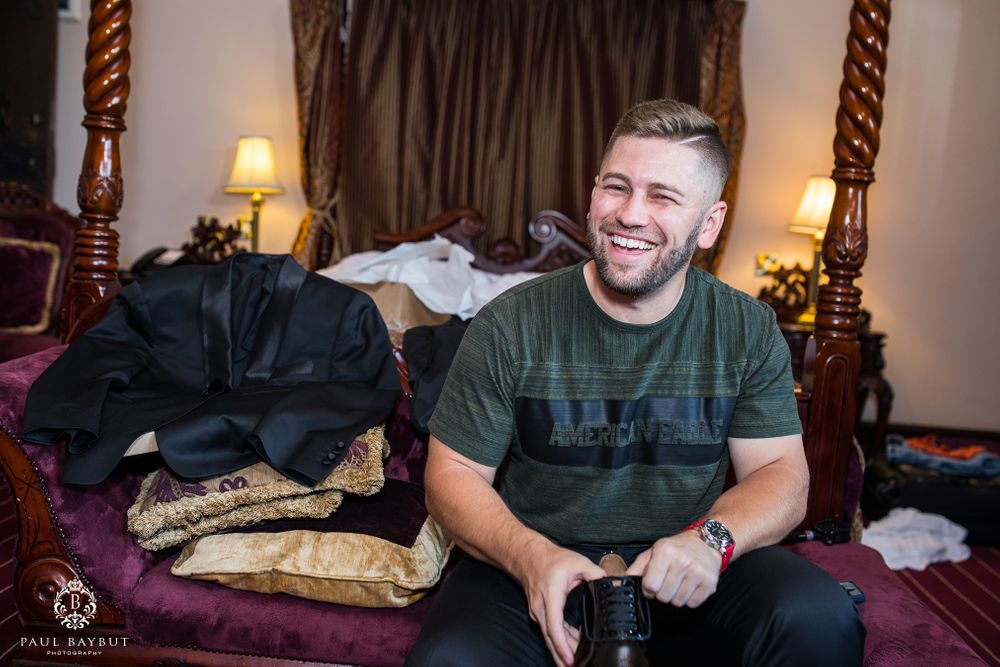 Casual person in green shirt smiles while sitting on bed during preparation time.