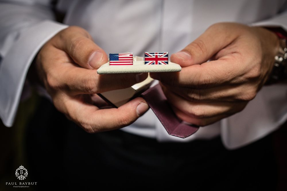 Hands hold American and British flag pins during wedding preparations.