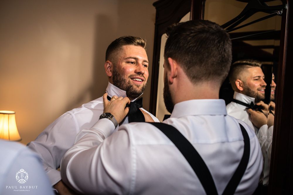 Person smiles while having bow tie adjusted in mirror reflection.