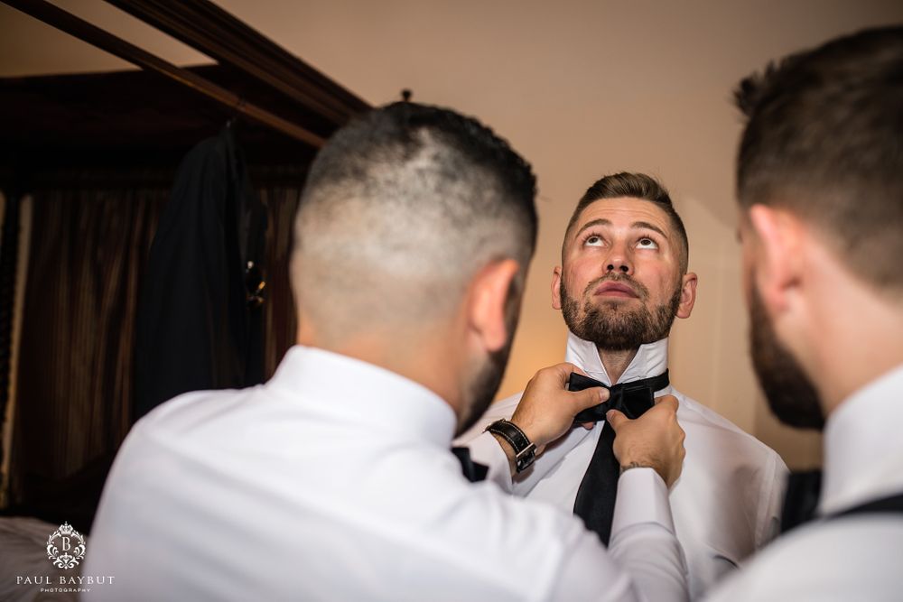 A wedding party helps adjust the groom's bowtie during preparation.