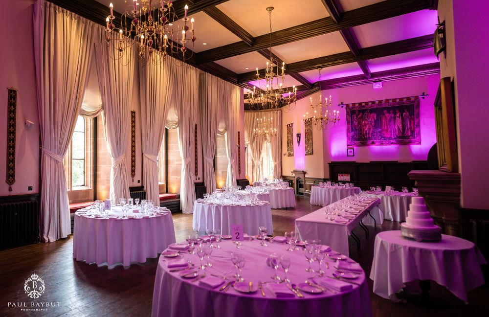 An elegant ballroom set for a wedding reception with purple lighting and round tables.