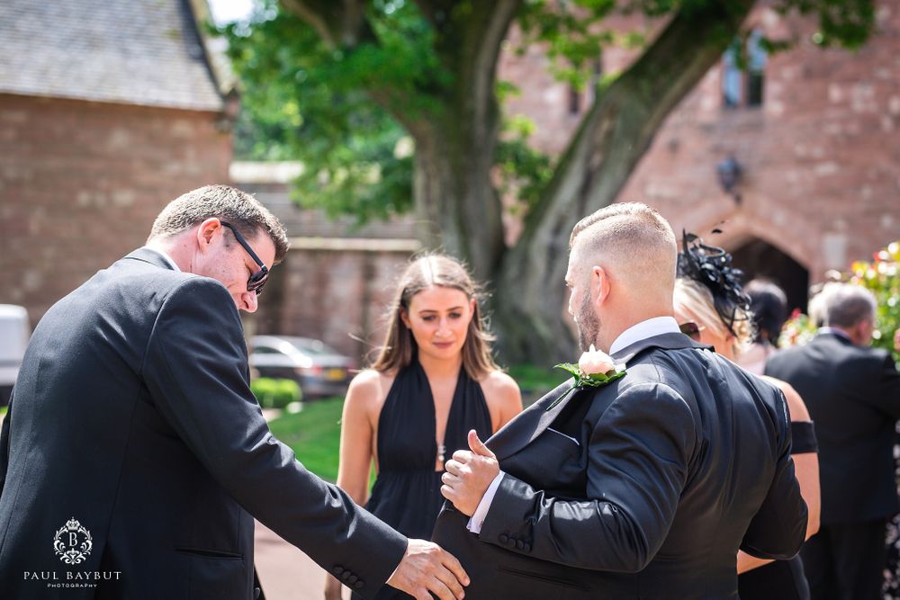 Outdoor gathering with people in formal attire conversing near a stone church building.