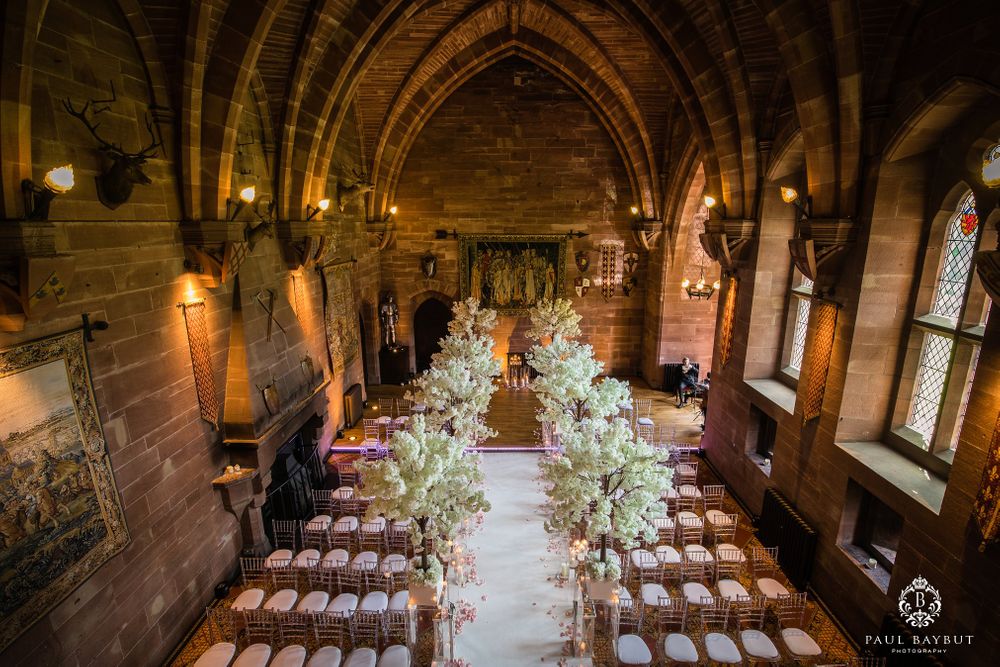Gothic stone chapel interior with elegant wedding ceremony setup featuring floral aisle decorations.