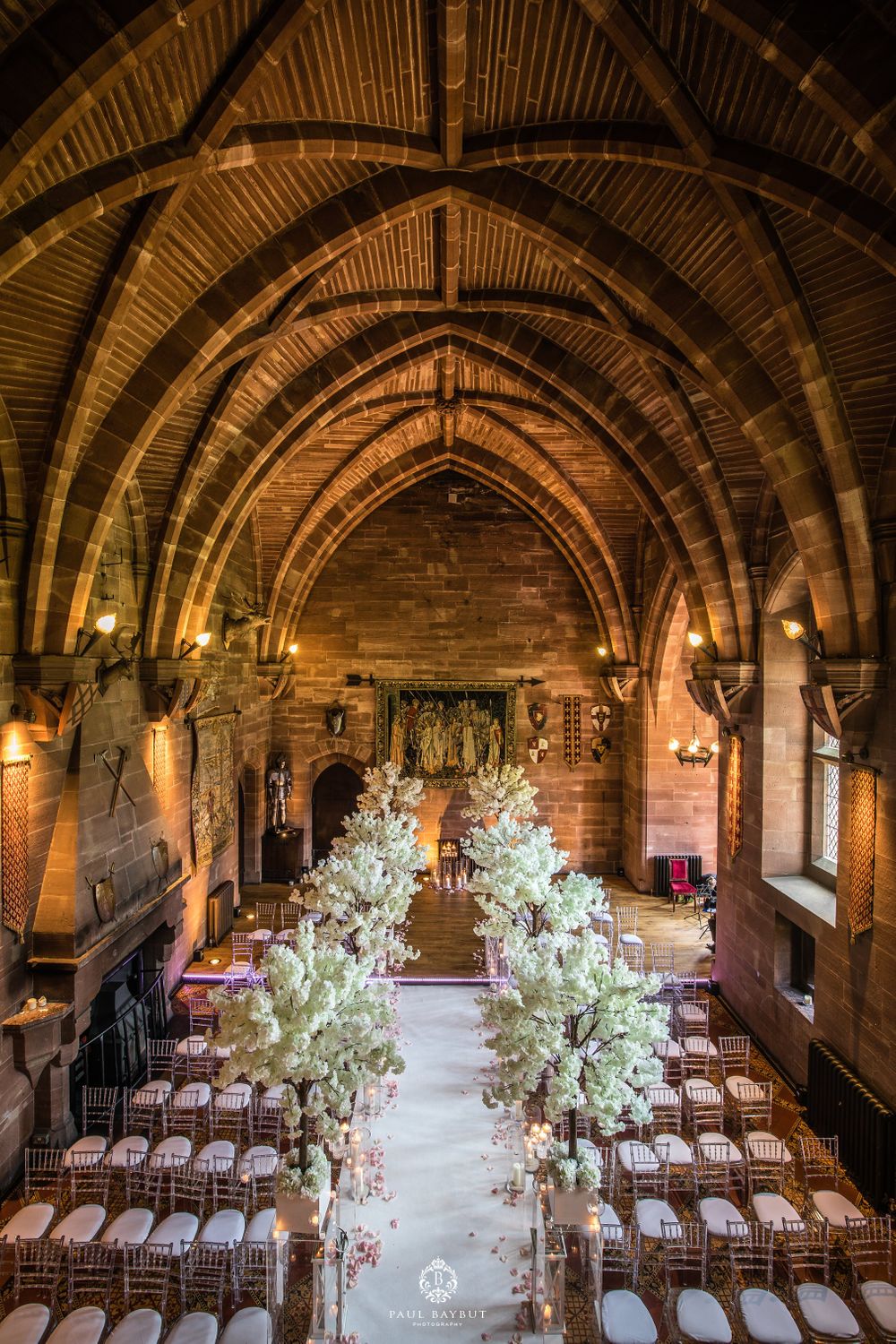 Gothic chapel interior with dramatic arches and white floral aisle decorations for wedding ceremony.