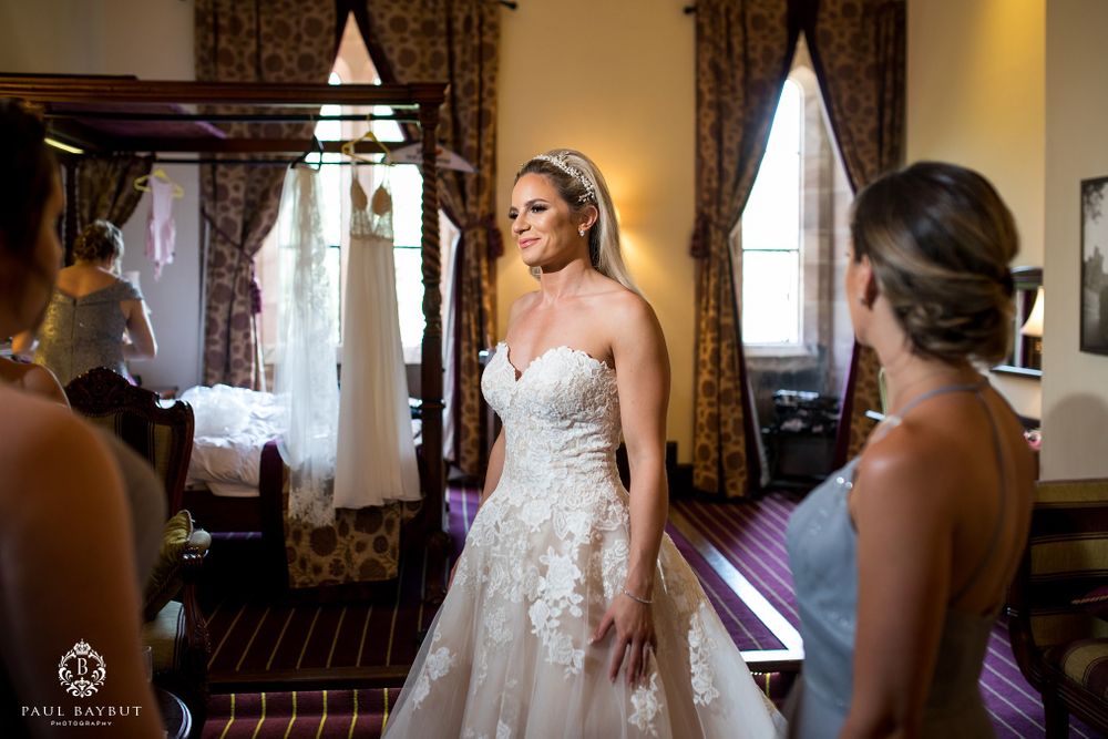 Wedding dress fitting session in elegant room with ornate mirror and curtains.