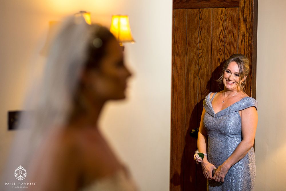 A silhouetted figure in bridal attire with someone in blue dress visible through doorway.