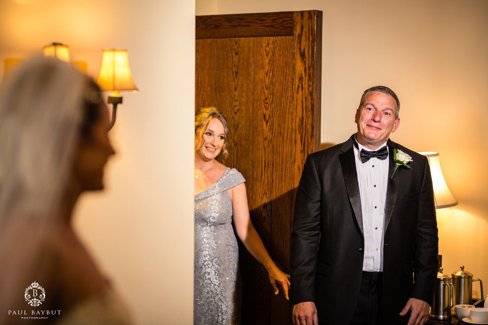 Wedding party members react with joy during a first look moment in an elegant room.