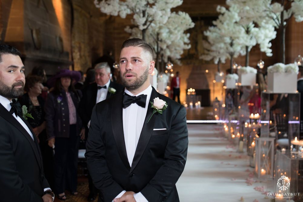 Wedding ceremony in historic church decorated with towering white floral arrangements and candle-lit aisle.
