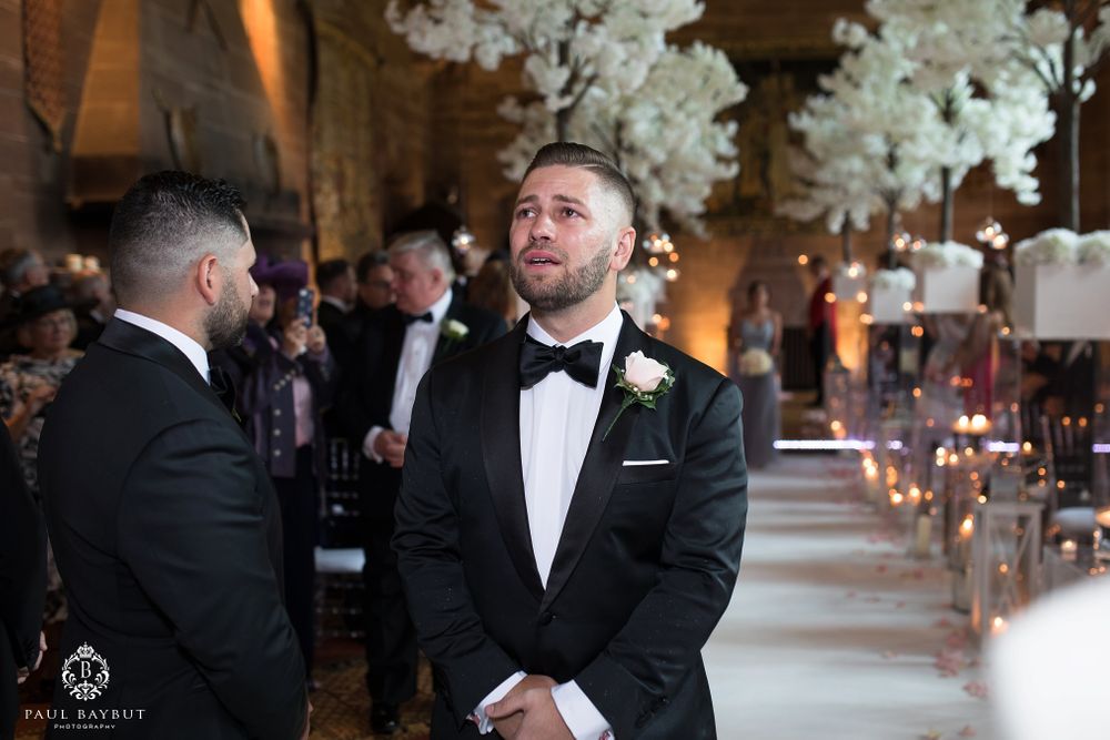 Candid moment during wedding ceremony in ornate church with dramatic floral decorations.