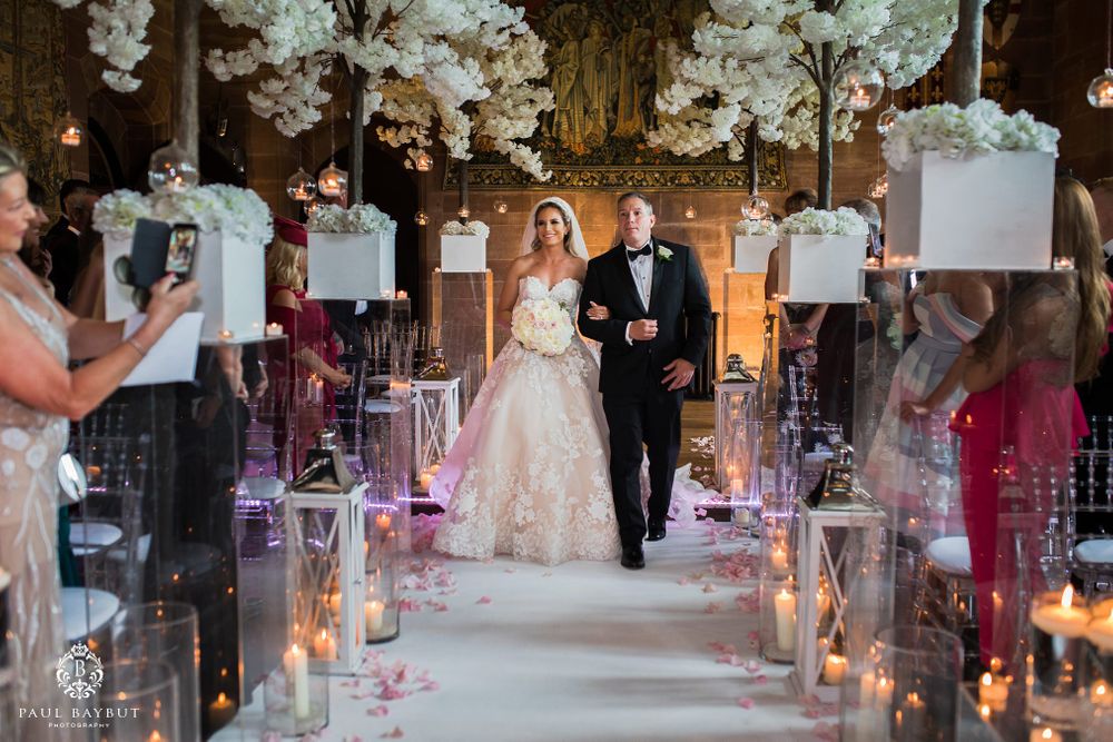 Couple walking down candlelit aisle decorated with white cherry blossom trees in grand church setting.