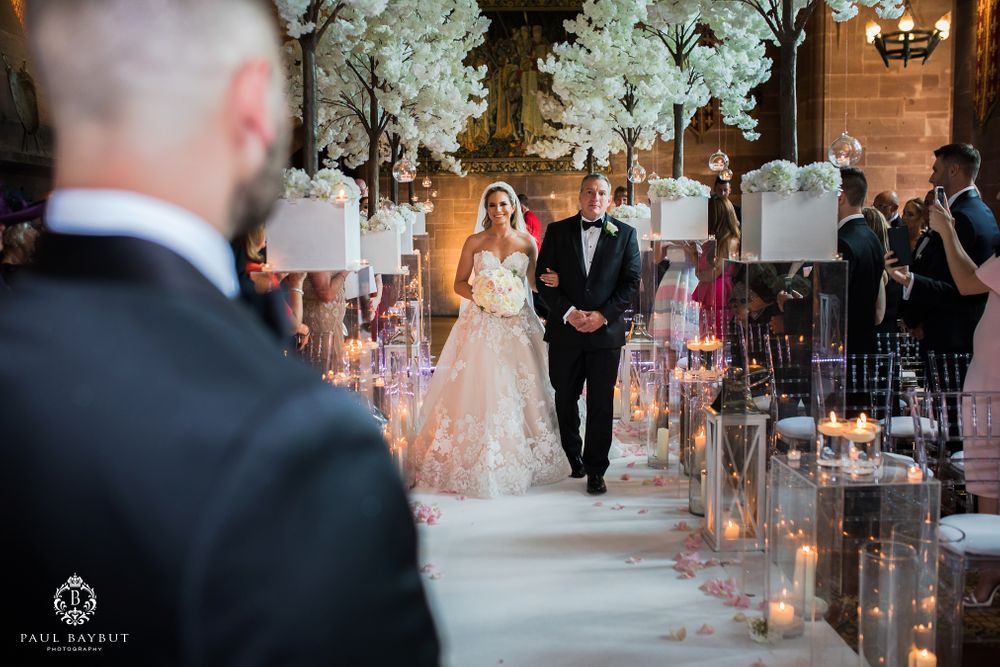 Couple proceeds down candle-lined aisle decorated with white cherry blossom trees during church ceremony.