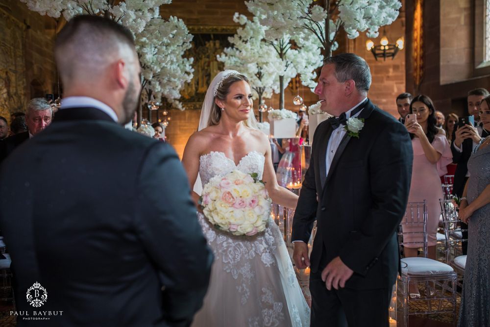 Elegant wedding ceremony with white floral decor and couple exchanging vows in ornate venue.