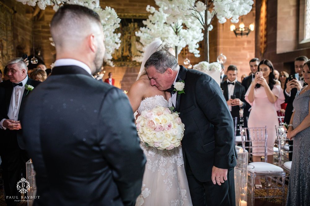 Emotional wedding ceremony moment captured in elegant venue with white floral decorations.