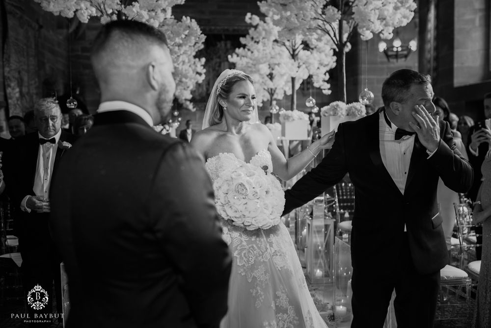 Wedding party during ceremony with dramatic white floral arrangements in background.