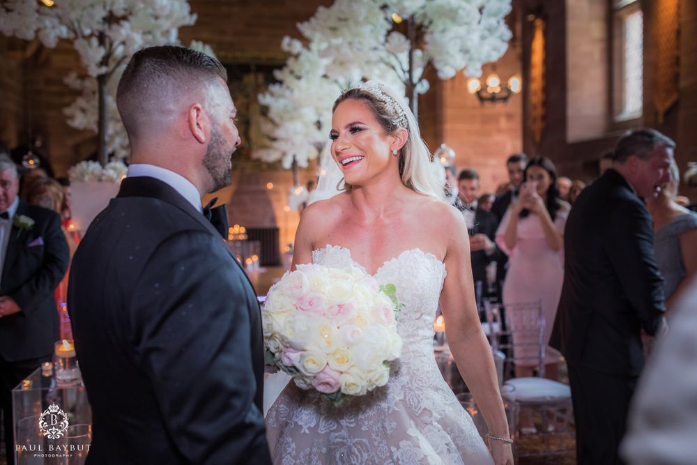 Wedding ceremony with bride holding white bouquet in venue decorated with floral arrangements.