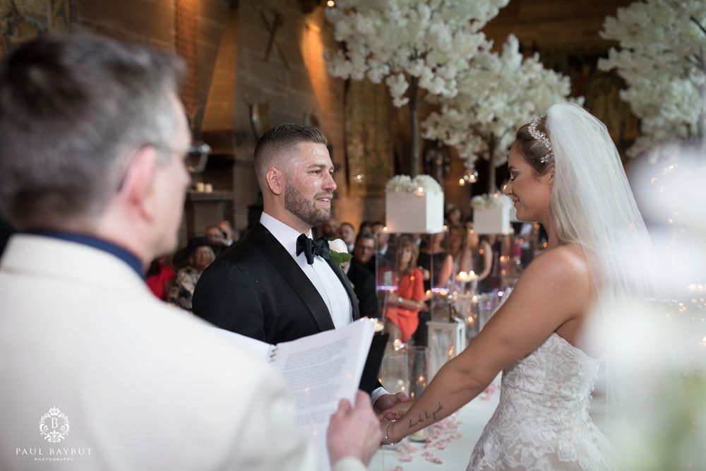 Wedding ceremony features groomsmen in black tuxedos standing at attention.