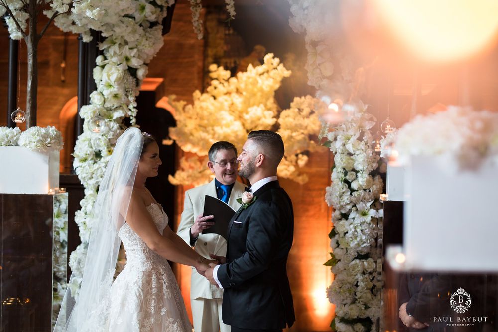 A romantic wedding ceremony moment captured in warm lighting under white floral arrangements.