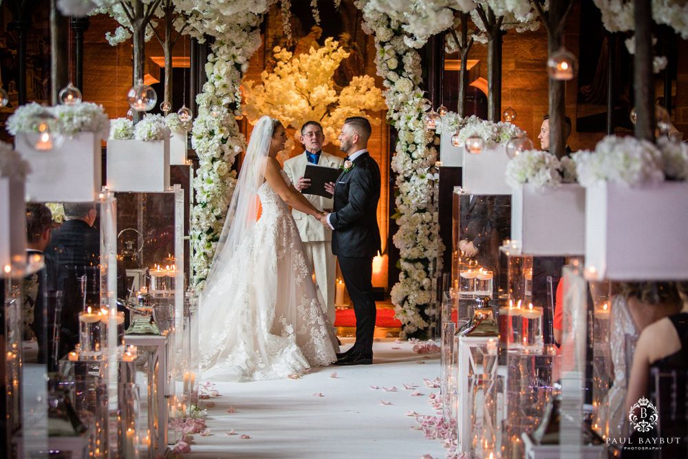 A wedding ceremony aisle lined with candles and white floral arches creates a romantic atmosphere.