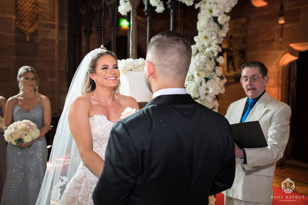 A tender moment during wedding vows beneath an arch of white flowers and elegant decor.