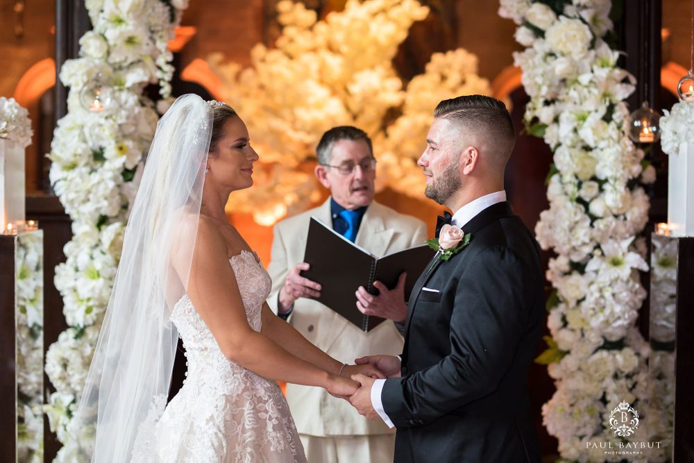 Elegant wedding ceremony with white floral arches and warm lighting during the vow exchange.
